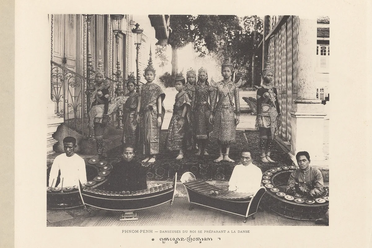 An early black-and-white postcard of Cambodian court dancers in costume behind a row of seated musicians with xylophone-type instruments.