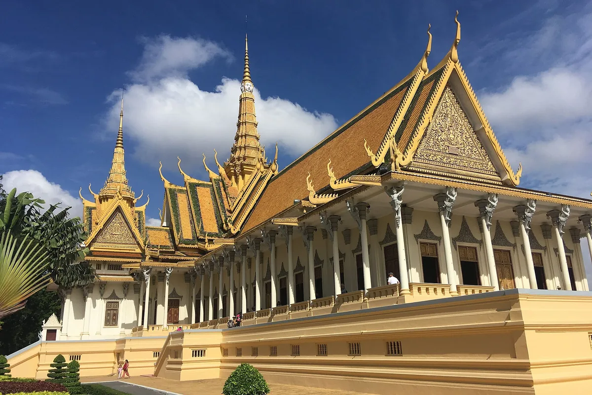 The gilded roofs and spires of the Throne Hall at the Royal Palace in Phnom Penh under a blue sky.